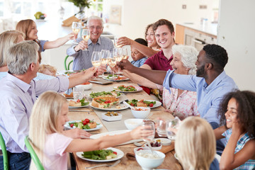 Group Of Multi-Generation Family And Friends Sitting Around Table And Making A Toast