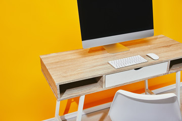 close up of workplace with computer and wooden table near yellow wall