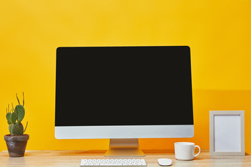 Computer, cactus in pot and cup of coffee at wooden table on yellow