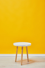 Minimalistic little wooden table near yellow wall - obrazy, fototapety, plakaty