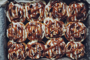 Traditional cinnamon buns with pecan nuts and caramel sauce in baking paper, top view