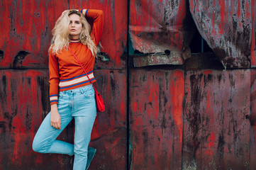 Fototapeta na wymiar Lifestyle fashion portrait of young beautiful cute girl model. Odd bizarre strange unusual cute naughty blonde babe posing on old rusty metal gate background. Nice looking woman in trendy clothes.