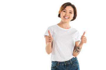 smiling young woman showing thumbs up signs and looking at camera isolated on white