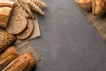 Bread background with wheat, aromatic crispbread with grains, copy space, top view. Brown and white whole grain loaves still life composition with wheat ears scattered around.