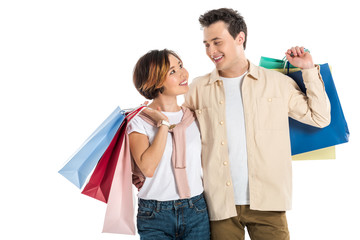 smiling couple looking at each other and carrying shopping bags isolated on white