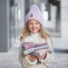 Cute little girl in a knitted lilac hat holding a new knitted hats and laughing