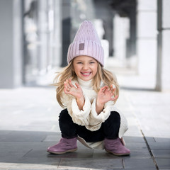 Cute little girl in a knitted lilac hat holding a new knitted hats and laughing