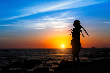 Fototapeta na wymiar Silhouette of young woman on the sea coast during amazing sunset.