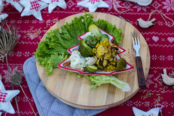 Christmas tree form dish plate with mixed vegetables, curry risotto rice and avocado. Vegan lunch, vegetarian dinner, healthy food. Red tablecloth