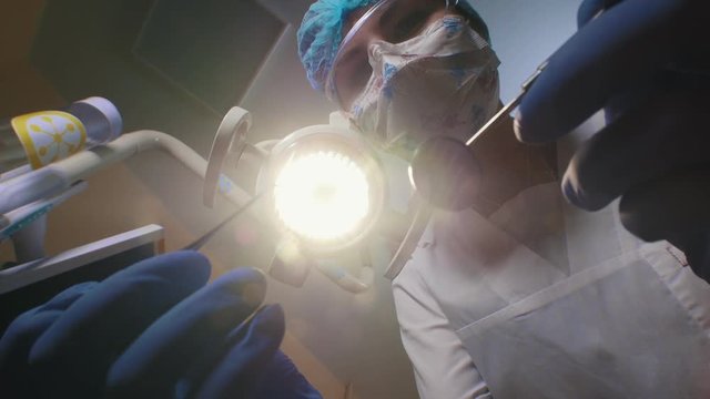 A dentist turns on the lamp and coming closer to the patient holding tools. First person shooting