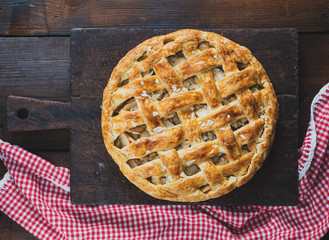 Baked whole round apple pie on a rectangular old brown board
