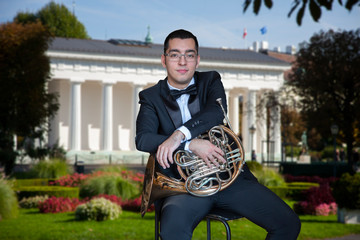 French horn player. Hornist playing brass orchestra music Portrait on the background of the city