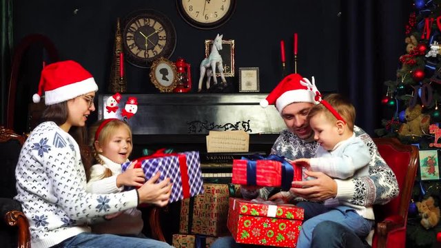 Happy adorable two kids family gathered in lovely Christmas decorated living room to open surprise presents from Santa