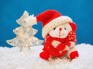 Cute white bear in red hat of Santa Claus and shining fir tree 