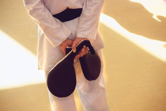Karate trainer in kimono with a kicking targets pad in his hands in the gym during training