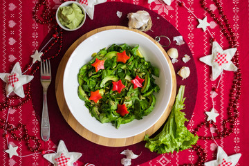 Spinach avocado fresh salad with Christmas red stars. Christmas food on red teblecloth