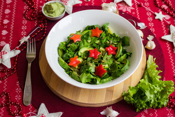 Spinach avocado fresh salad with Christmas red stars. Christmas food on red teblecloth