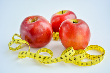 Red juicy apples are on a white background, there is a bright yellow measuring tape around the apples.