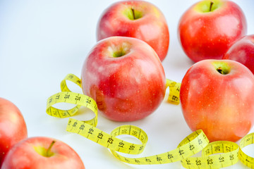 Red juicy apples are on a white background, there is a bright yellow measuring tape around the apples.