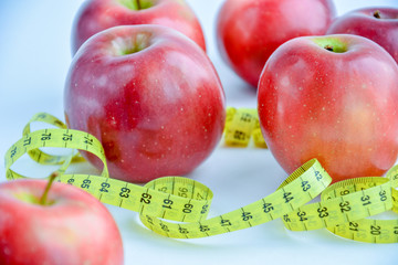 Red juicy apples are on a white background, there is a bright yellow measuring tape around the apples.
