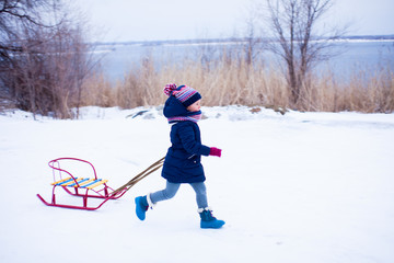 Little girl is running to the snow hill with her sledge