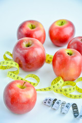 Red juicy apples on a white background, around the apples there is a bright yellow and black and white measuring tape.