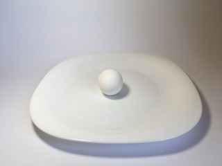 White egg on a white plate on a white background. The birth of life. Chicken egg.