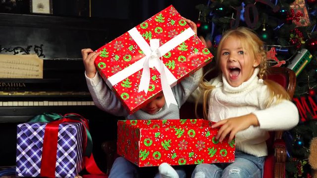 Adorable surprised kids under Christmas tree open big bright wrapped gift box filled with candy cane presents from Santa