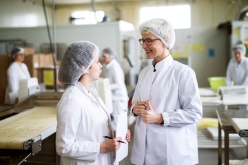 Two female workers discussing while standing in food factory.