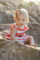 One-year-old baby girl in a red and white dress sitting on the rocky coast, spending time outdoors is important for little ones