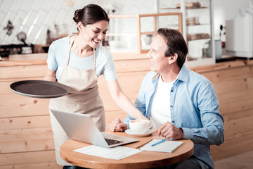 Joyful nice woman putting a cup of coffee on the table
