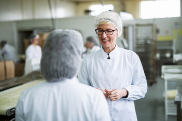 Two female workers discussing about food quality while standing in food factory.