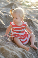 One-year-old baby girl in a red and white dress sitting on the rocky coast, spending time outdoors is important for little ones