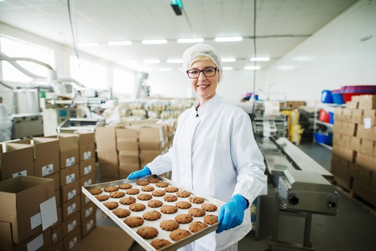 Female worker standing and holding plate with cookies.
