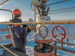 The operator services an oil well in the northern oil field in winter. The equipment for oil production is covered with ice.