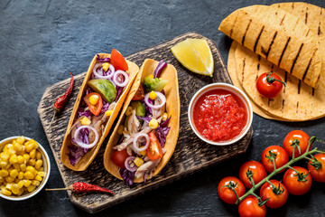 Tacos with chicken, vegetables and salsa sauce in tartilla on dark background