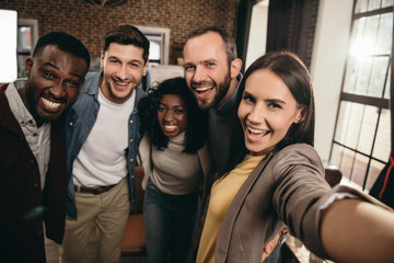 camera point of view of group of cheerful coworkers taking selfie using smartphone