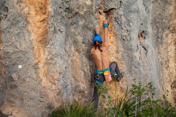 Shirtless climber man climbing mountain wall on amazing sunny day