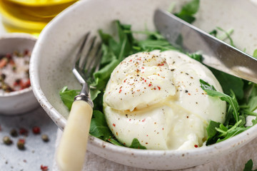 Delicious Creamy Italian Burrata Cheese Served with Olive Oil, fresh arugula and spices in a white plate © la_vanda