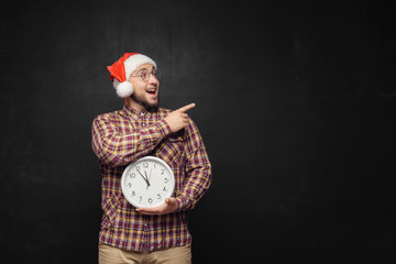 Christmas men with clock. Portrait of surprised young man wearing red santa claus hat, holding...