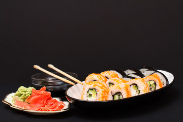 Uramaki California. Sushi rolls and bowl with soy sauce on black background.