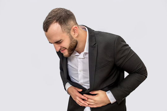 Businessman suffers from pain in stomack area. He holds both hands there and look down. Isolated on white background.