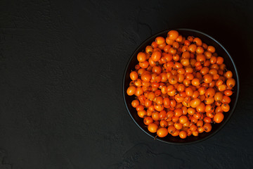 Sea buckthorn. Ripe fresh berries in bowl on black concrete background. Top view