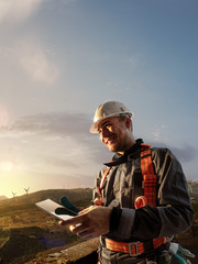 Heureux ingénieur planifiant un nouveau projet. Il se tient debout sur un support supérieur et regarde dans une tablette. autour de beaux paysages