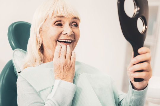 Mature woman with mirror looking at her denture