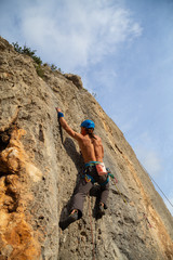 Shirtless climber man climbing mountain wall on amazing sunny day