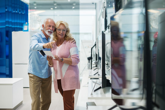 Happy senior couple choosing which television set to buy. Tech store interior.