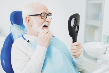 Appealing senior man evaluating his teeth