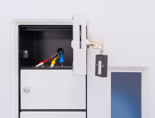Open storage box with chargers for cell phone. Locker key in open door.