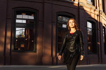Young smiling woman walking on the street on brown bricks wall background. Smiling girl in black